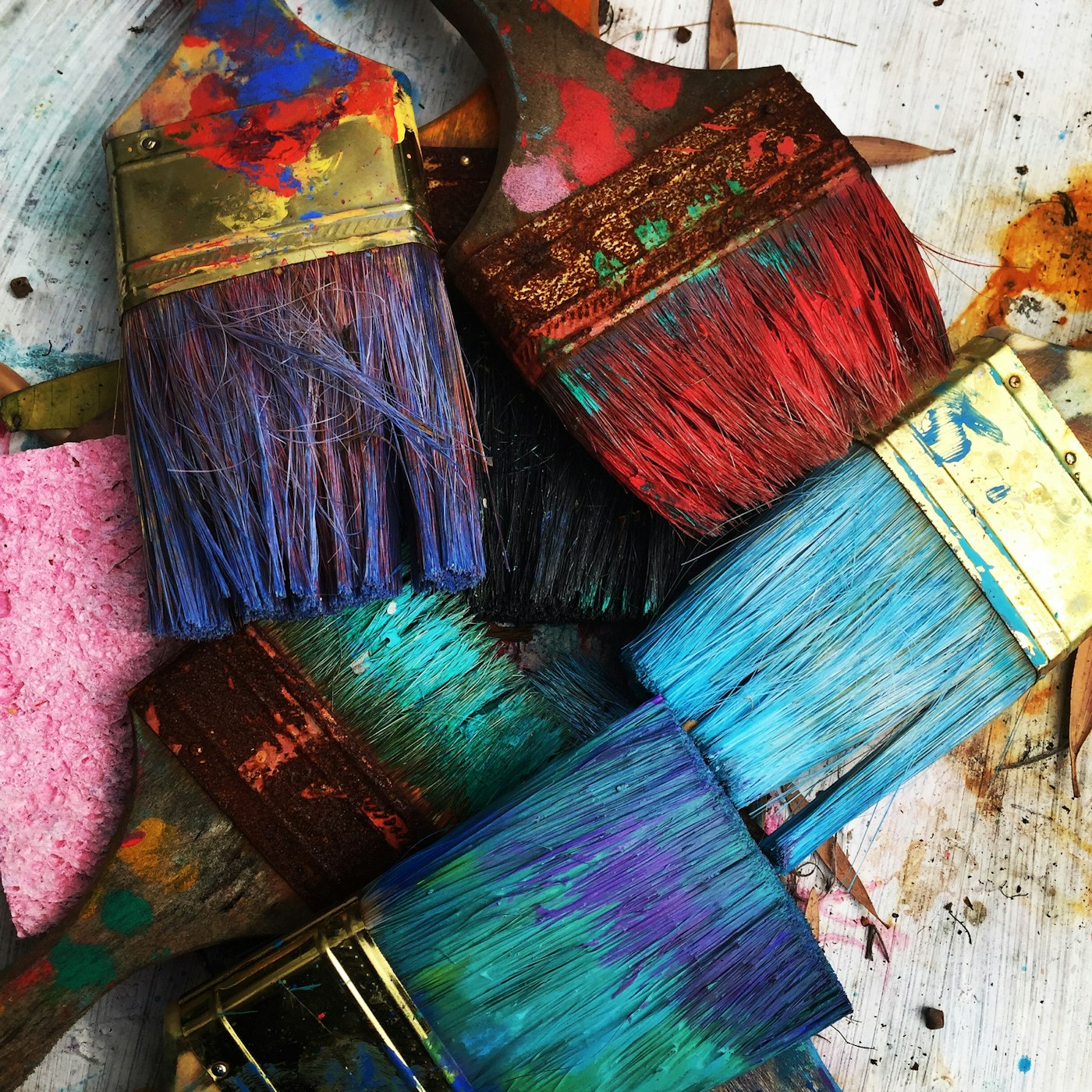 Paint-splattered brushes with blue, red, and turquoise bristles on a work surface