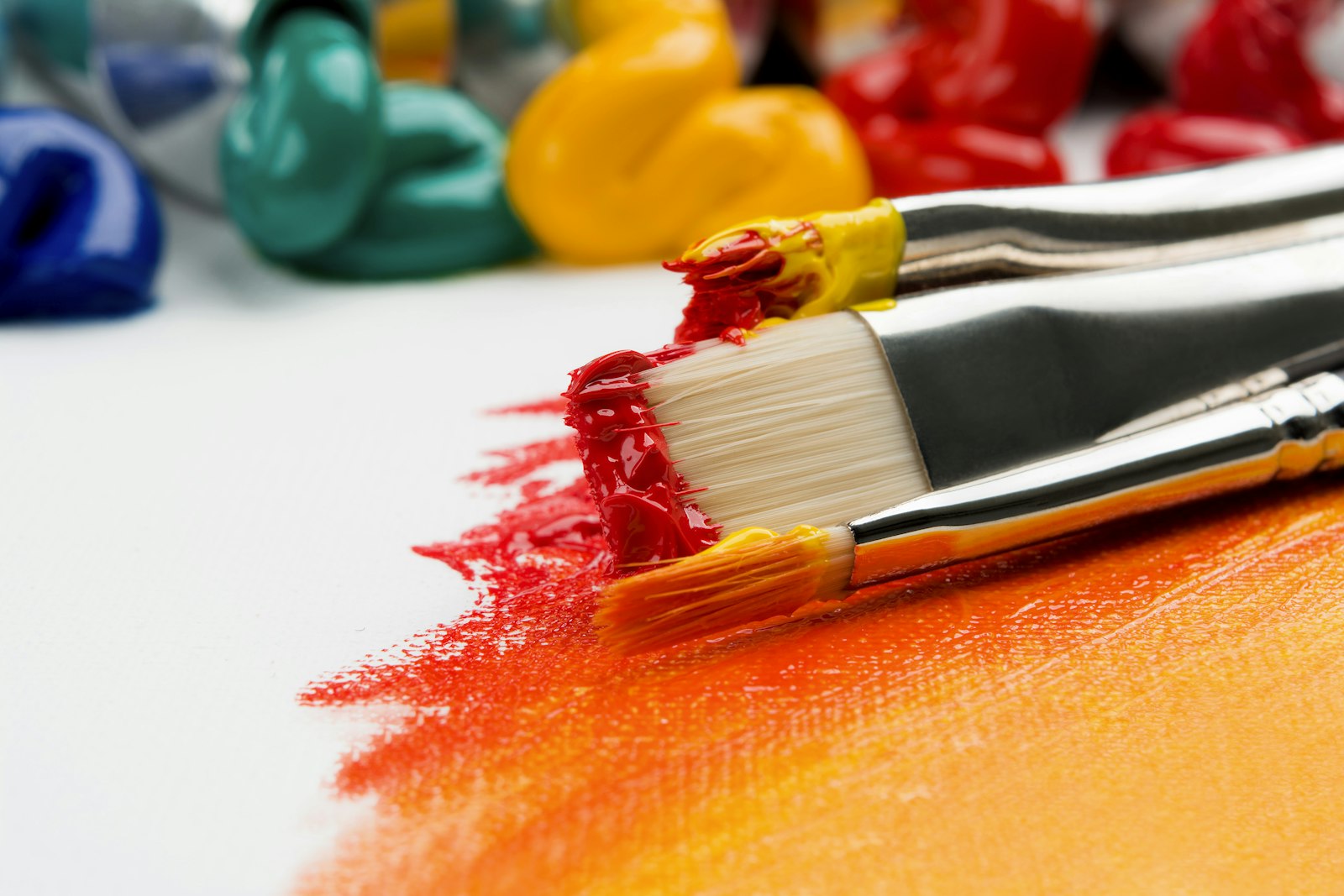 Paintbrushes with red and yellow paint on a white canvas