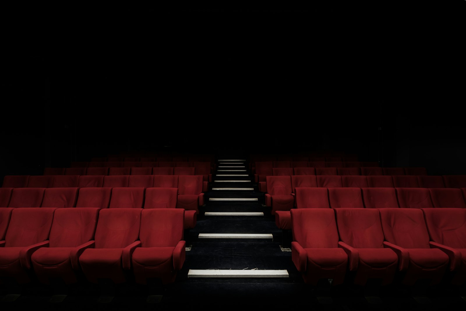 Dim cinema seating with lit aisle steps leading toward the screen